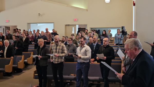 Pastors and church members standing together with service sheets during a Confessing the Faith 2026 session