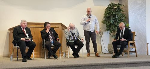 Panel of speakers seated on the platform during the question-and-answer session, with a moderator standing to relay a question