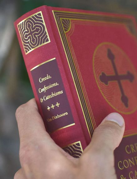 Hand holding Creeds, Confessions & Catechisms by Chad Van Dixhoorn